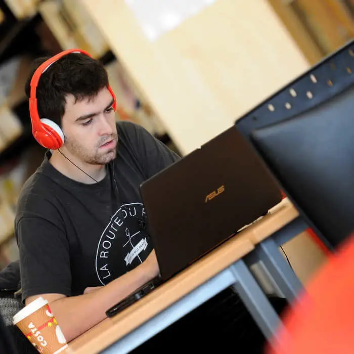 male students with headset working on a laptop in the library of ϲϿ